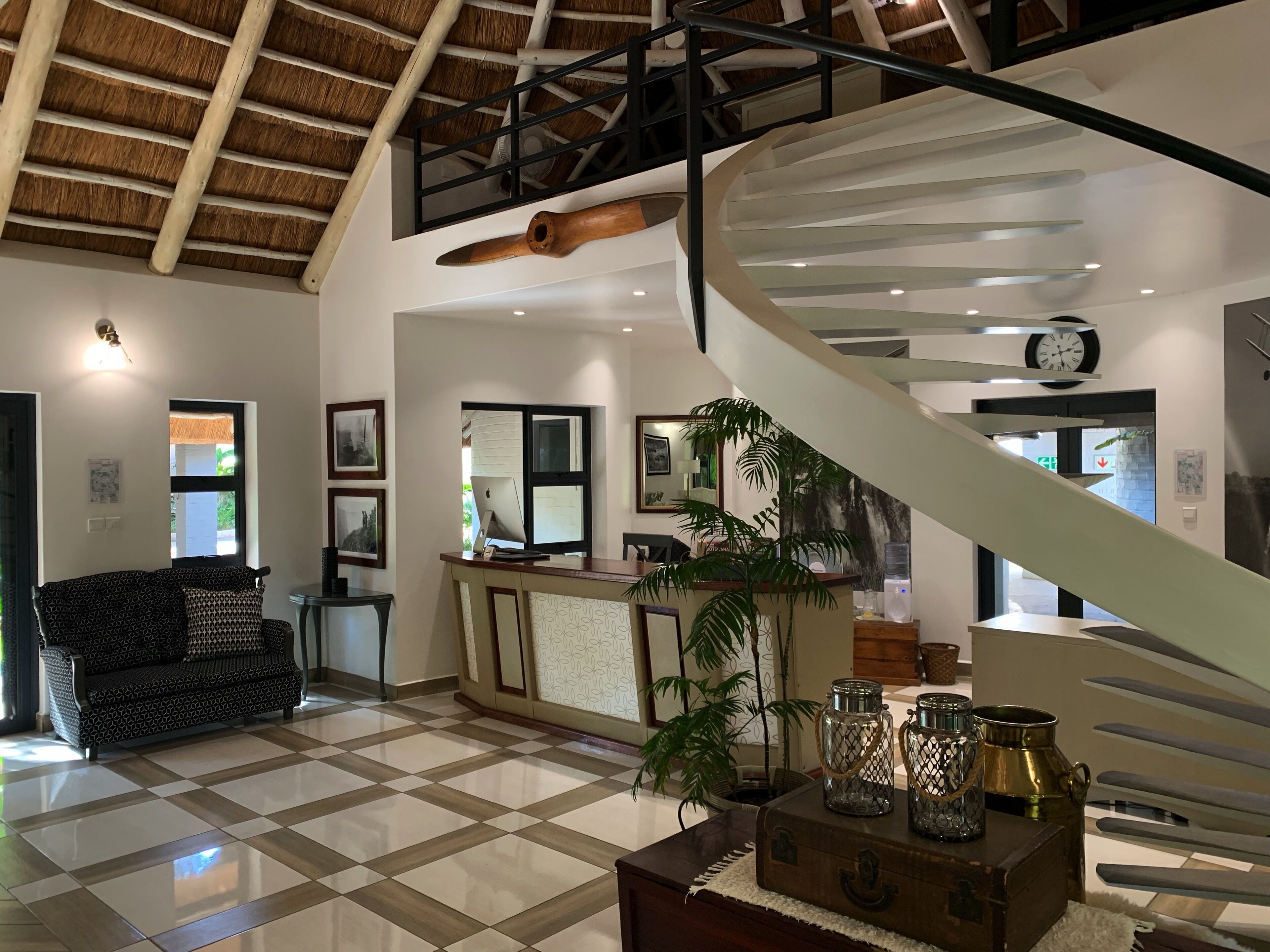 A spacious lobby with a checkered floor, a staircase, a reception desk, and a large potted plant.