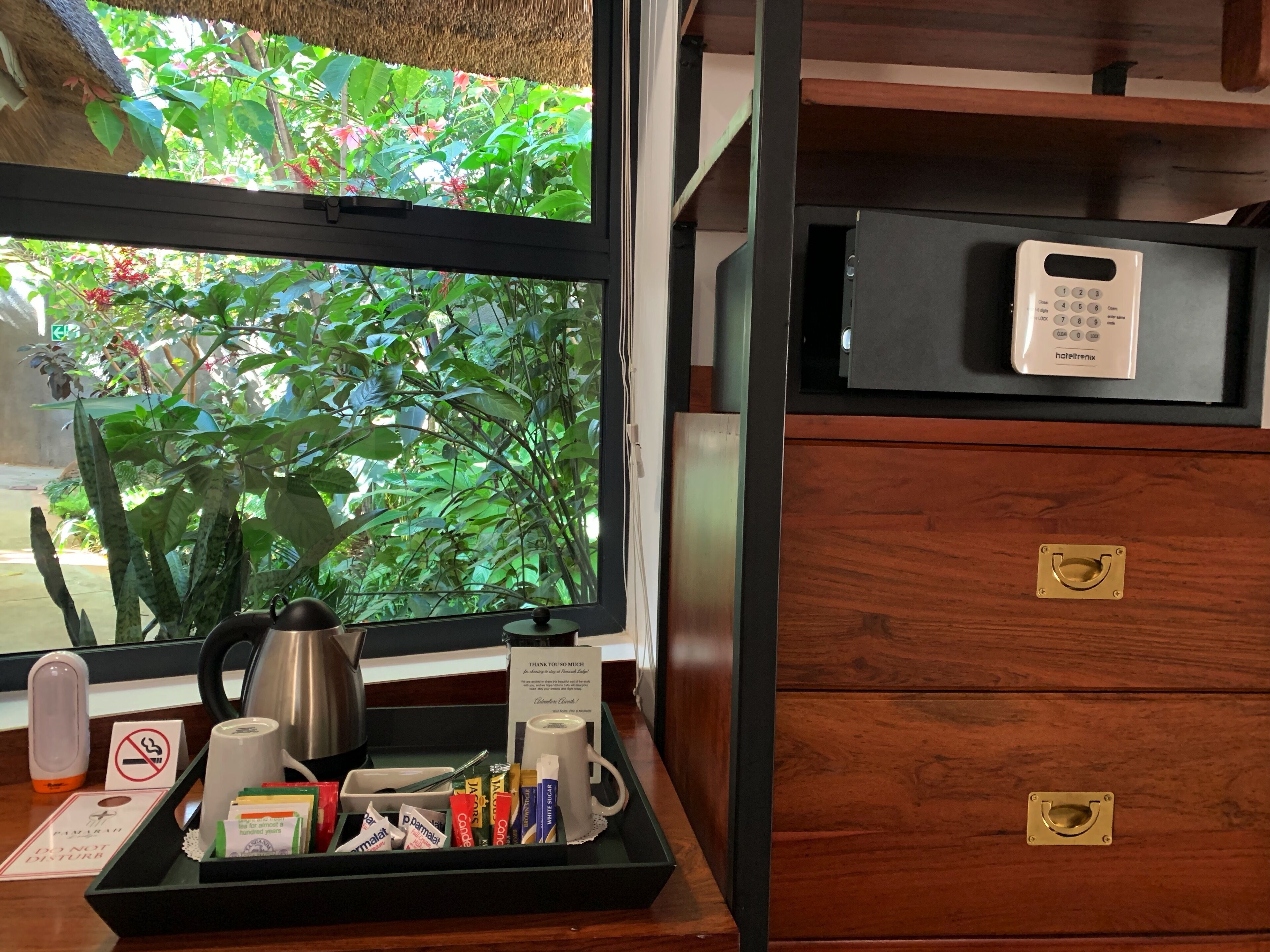 Habitación de hotel con escritorio de madera, bandeja con artículos de aseo, ventana con vistas a zonas verdes y minibar con llave.