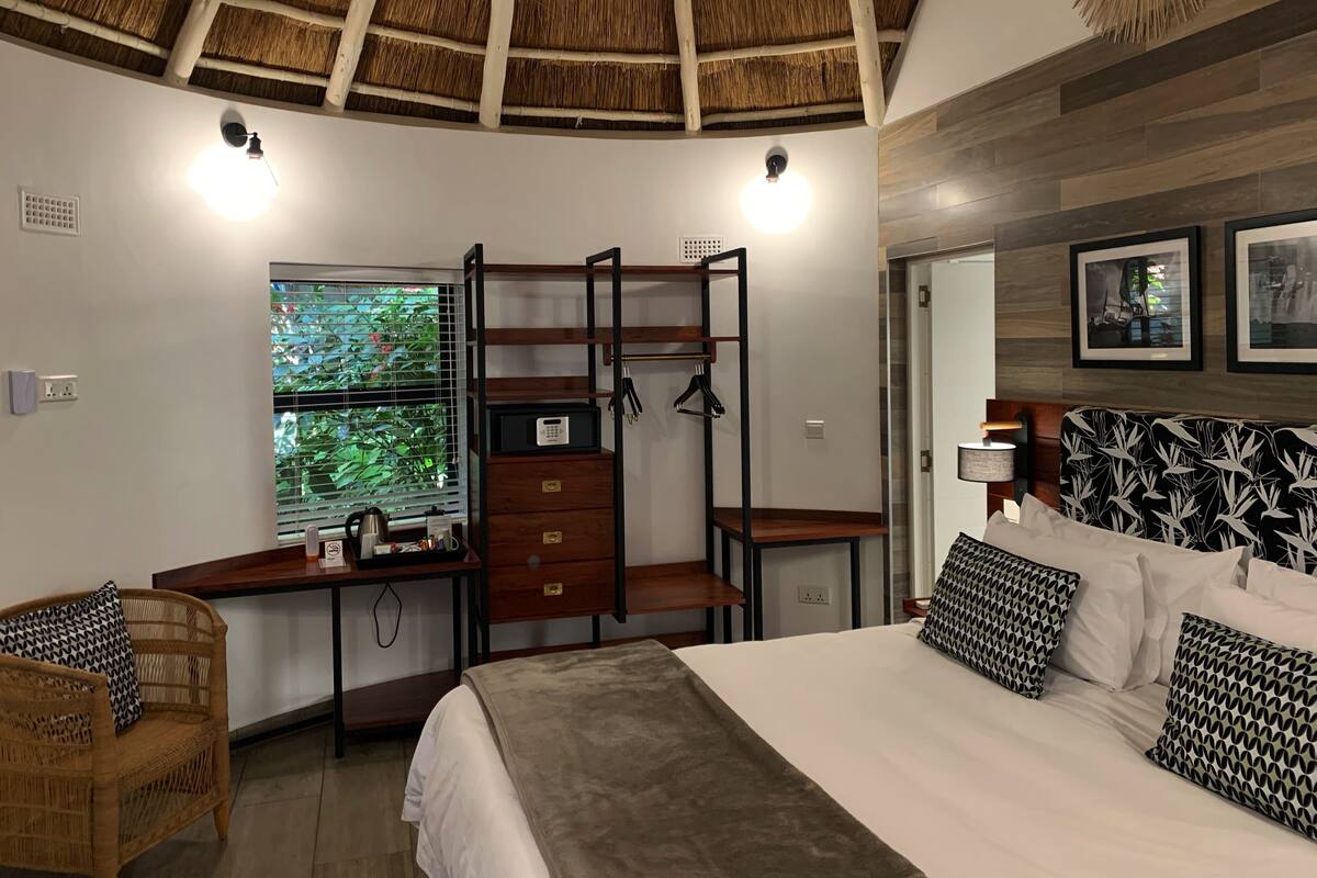 A bedroom with a bunk bed, a desk with a computer, a window with blinds, and a bed with patterned pillows.