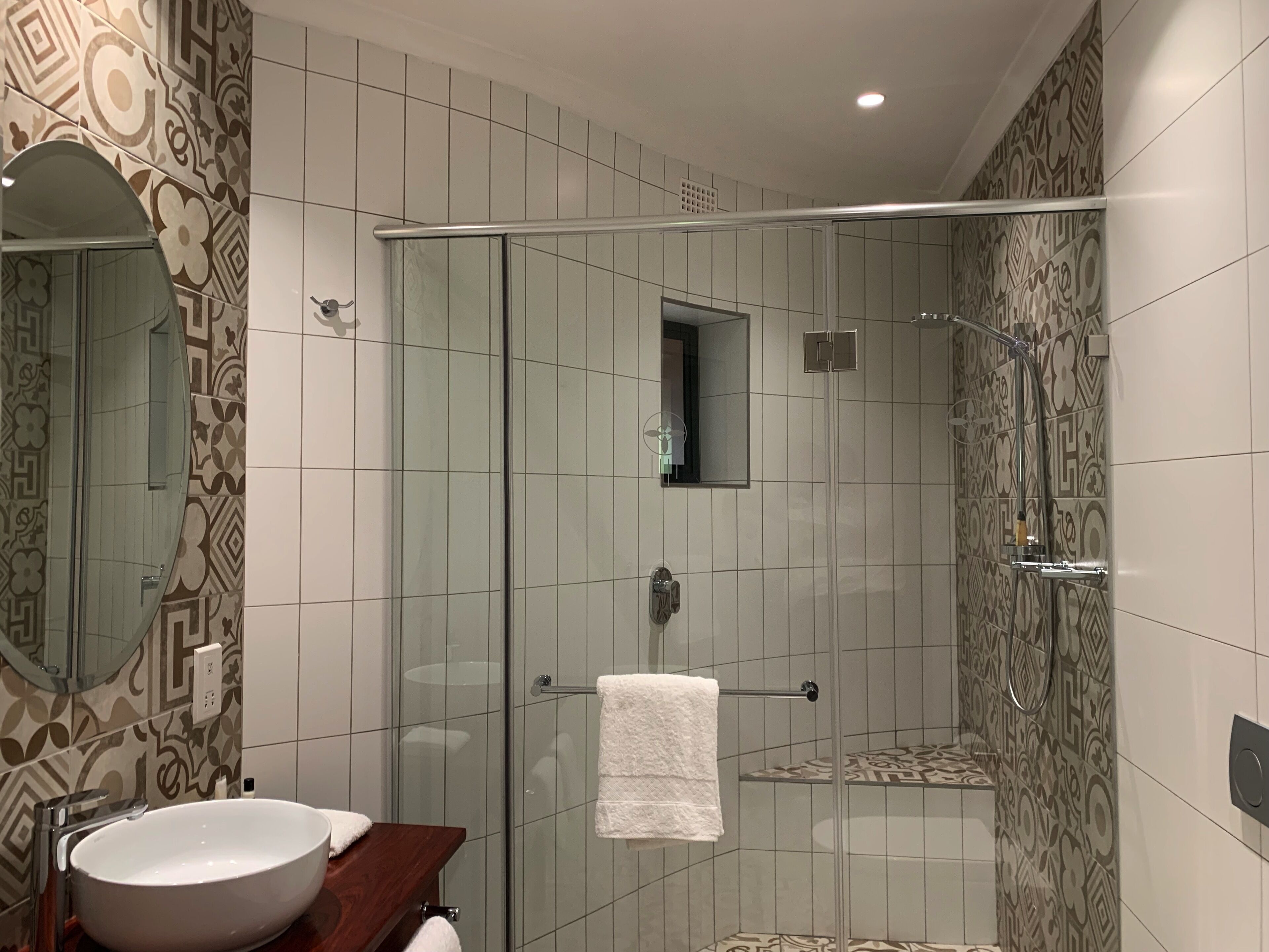 Ein modernes Badezimmer mit einer gläsernen Duschkabine, einem großen Spiegel und strukturierten Fliesen.