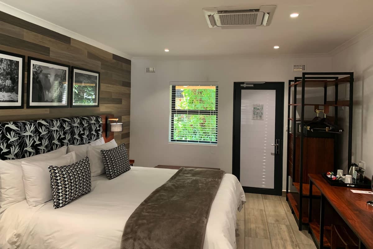 A hotel room with a bed, a bedside table, a wardrobe, and a window with blinds.