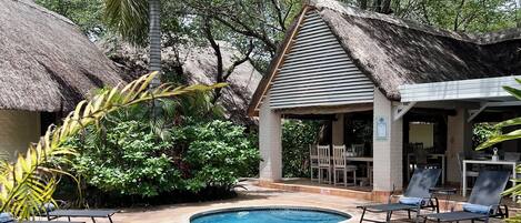 A swimming pool with lounge chairs, a thatched-roof structure, and lush greenery.