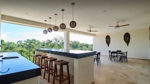 A spacious room with a kitchen island, bar stools, ceiling fans, and a dining area with chairs. - Sherlock - Swim up Suite & Gym & Beach Club Access (Tulum)