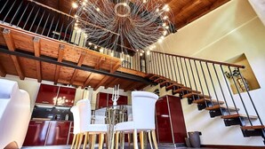 A modern interior with a staircase, wooden beams, and a dining area with white chairs. - Luxury Design Loft - [Piazza Pontida] (Bergamo)