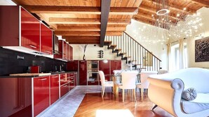 A modern kitchen with red cabinetry, a dining area with white chairs, and a staircase leading to an upper level. - Luxury Design Loft - [Piazza Pontida] (Bergamo)