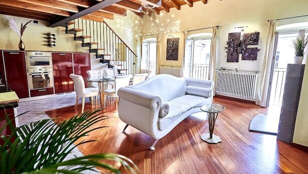 A spacious living area with a white sofa, wooden floors, a staircase, and a kitchen in the background. - Luxury Design Loft - [Piazza Pontida] (Bergamo)