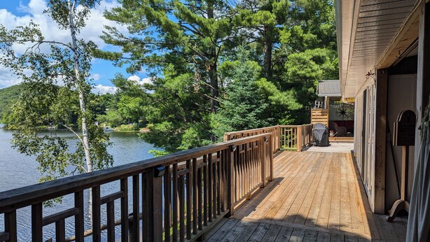 Une terrasse en bois avec une balustrade donnant sur un lac, entourée d’arbres.