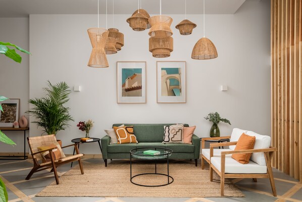 Un salón moderno con un sofá verde, sillas de madera, una mesa de centro de vidrio y lámparas colgantes tejidas.