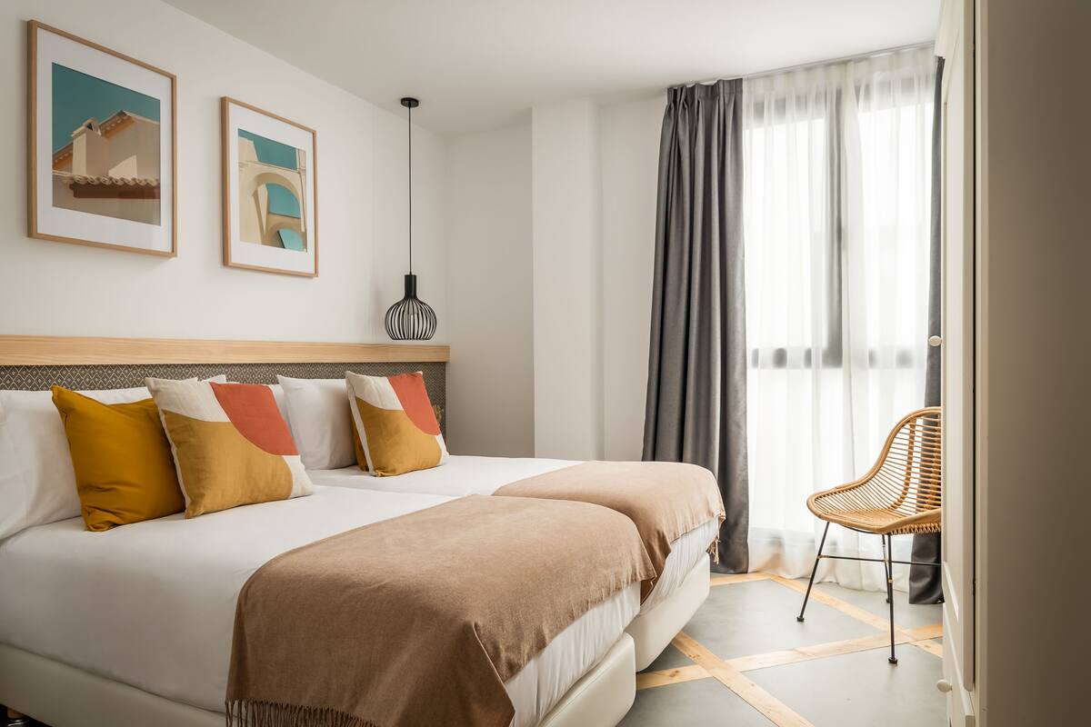 A hotel room with a large bed, two pillows, a chair, and a window with curtains.