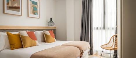 A hotel room with a large bed, two pillows, a chair, and a window with curtains.