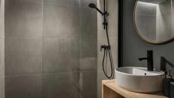 Un baño moderno con un espejo grande, un lavabo redondo y una ducha con cabezal de ducha manual.