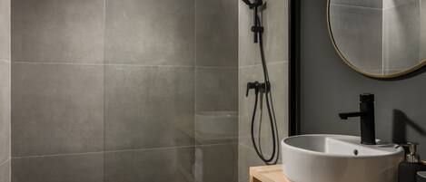 A modern bathroom with a large mirror, a round sink, and a shower with a handheld showerhead.
