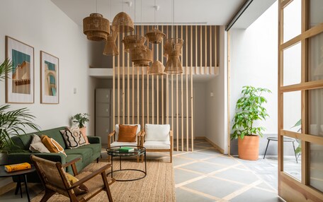 A modern living room with a green sofa, wooden chairs, a coffee table, and hanging wicker lamps.