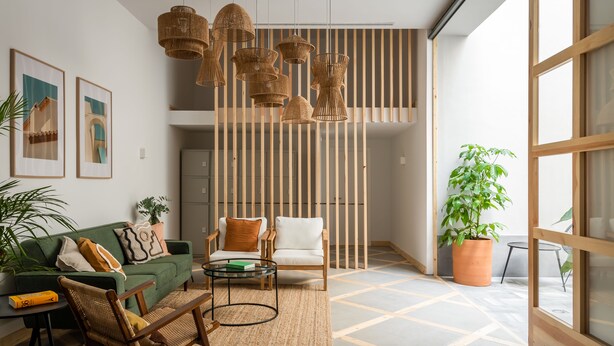 Una sala moderna con un sofá verde, sillas de madera, una mesa de centro y lámparas colgantes de mimbre.