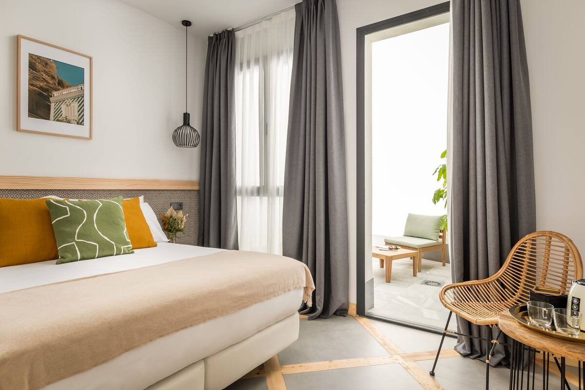 A modern hotel room with a bed, a dining area, and a view of the outdoors.