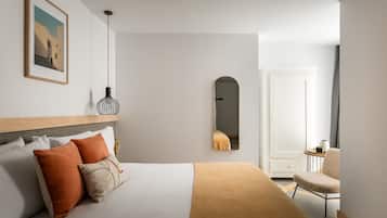 A modern bedroom with a bed, pillows, a bedside table, a chair, a mirror, and a framed picture on the wall.