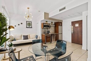 A modern living room with a glass dining table, a sofa, and a kitchen area with a microwave and oven.