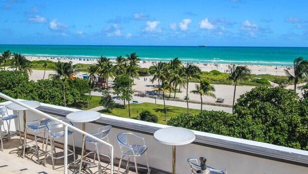A balcony with clear views of a beach and ocean, equipped with metal chairs and a small round table.