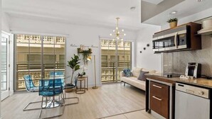 A modern kitchen with a built-in microwave, a dining area with blue chairs, and a large window with blinds.