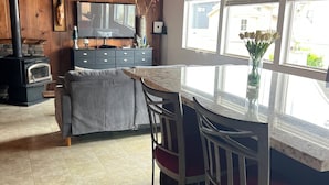 A cozy kitchen with a wooden interior, a central island with bar stools, a fireplace, and a large window. - Mckees Beach Cabin Steps From The Beach (Stanwood)