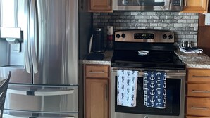 A kitchen with wooden cabinets, stainless steel appliances, a stone backsplash, and decorative fish sculptures. - Mckees Beach Cabin Steps From The Beach (Stanwood)