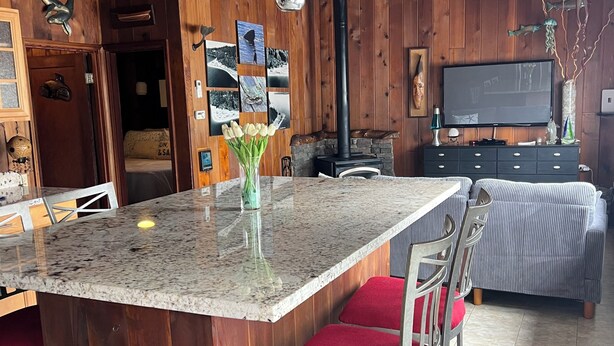 A wooden interior with a kitchen island, red cushioned chairs, a fireplace, and a television. - Mckees Beach Cabin Steps From The Beach (Stanwood)