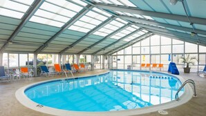 An indoor swimming pool with clear glass walls, a tiled floor, and multiple lounge chairs around the pool. - SRQ1 Enjoy unbeatable ocean views from the private balcony terrace, or oceanfront bedroom. (Kill Devil Hills)