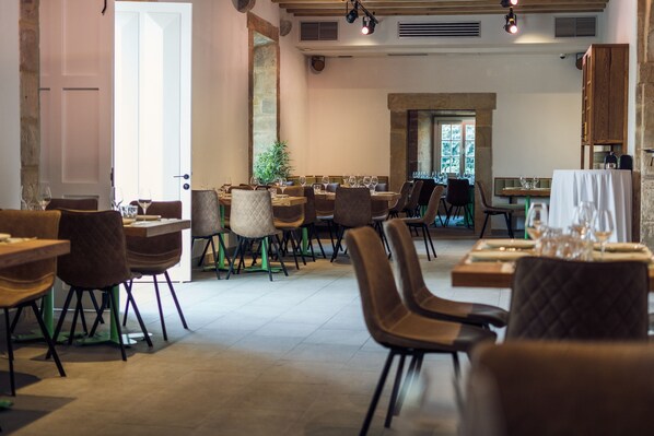 A restaurant with multiple dining tables and chairs, a stone wall, and a view of the outdoors. - Palacio de los Acevedo (Entrambasaguas)