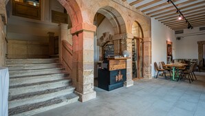 Una escalera de piedra que lleva a un nivel superior, una recepción con mostrador de madera y un comedor con sillas y una mesa.