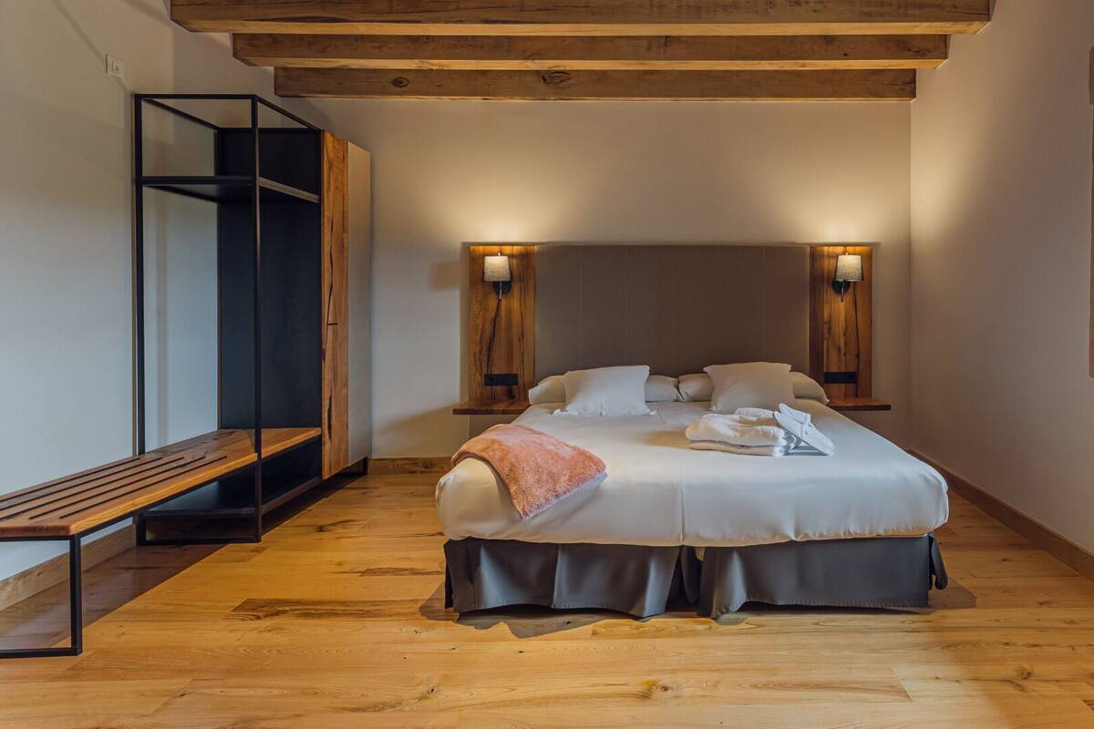 A bedroom with a bed, bedside lamps, a bench, and a window.