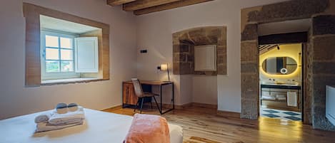 Un dormitorio con cama, escritorio, silla, ventana y baño con espejo y lavamanos.