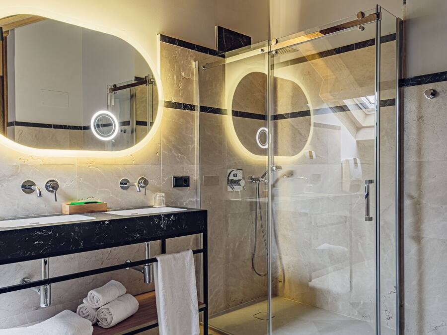 A modern bathroom with a glass-enclosed shower, a vanity with a marble countertop, and a large mirror with integrated lighting.