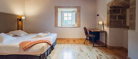 A bedroom with a bed, a desk, a chair, a window, and a stone wall.