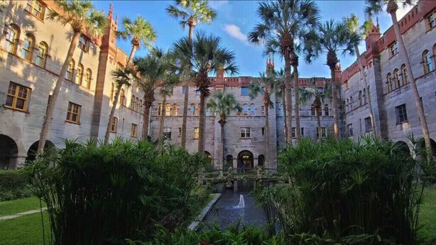A courtyard with a central water feature, surrounded by palm trees and a large building with arched windows and a symmetrical facade. - 3BR Modern Home in the Heart of St. Augustine (St. Augustine)