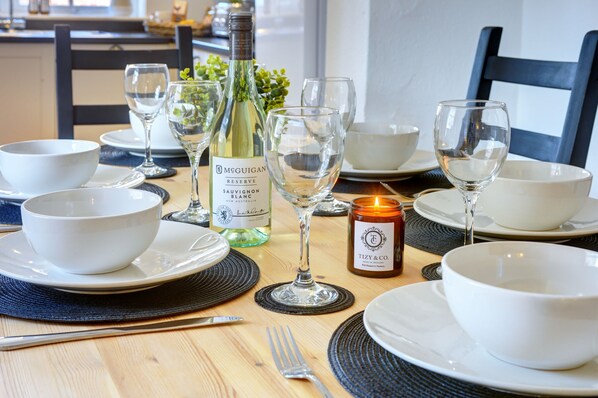 A dining table set with white bowls, plates, cutlery, wine glasses, and a bottle of wine.