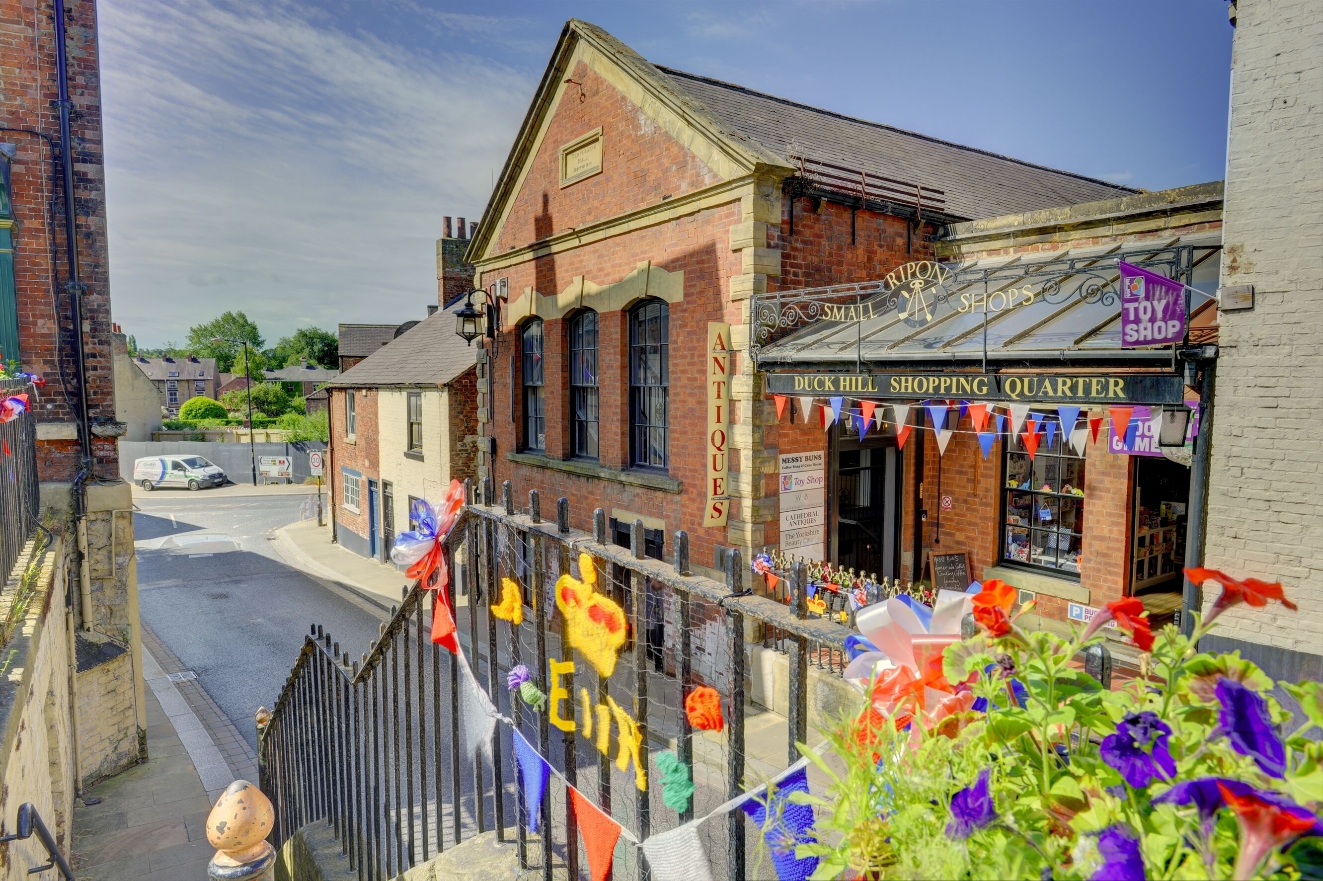 Vista de una calle con un edificio de ladrillo identificado como 'Duck Hill Shopping Quarter' y tiendas de 'Antigüedades'.