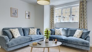 Ein Wohnzimmer mit zwei blauen Sofas, einem runden Couchtisch, einer Pflanze und einem Fenster mit Vorhängen.