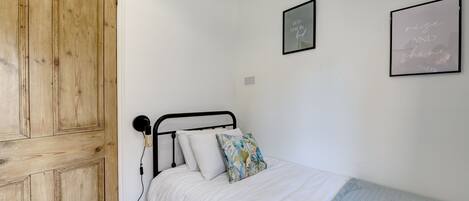 A bedroom with a wooden wardrobe, a bed with white bedding and a blue blanket, and two framed motivational quotes on the wall.