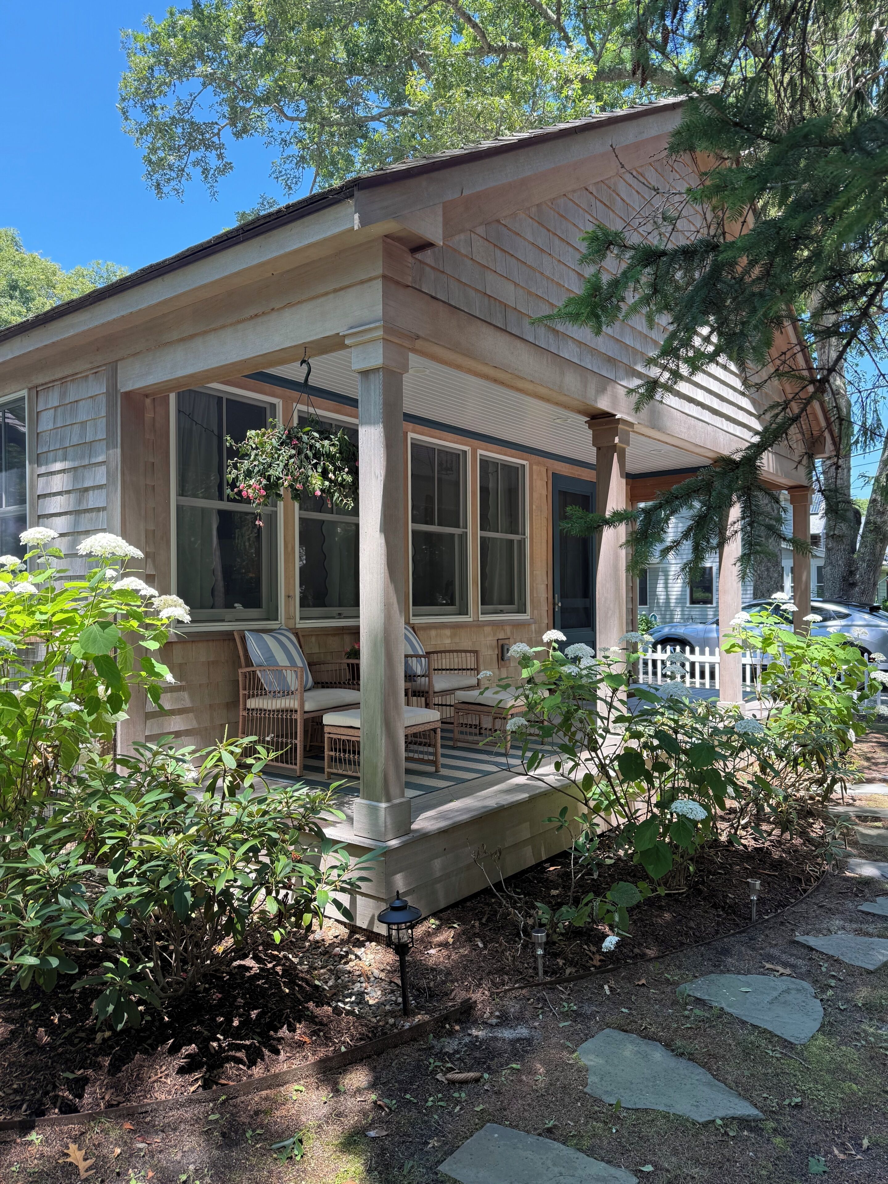 A covered porch with a seating area, a hanging flower basket, and a stone pathway leading to the house.