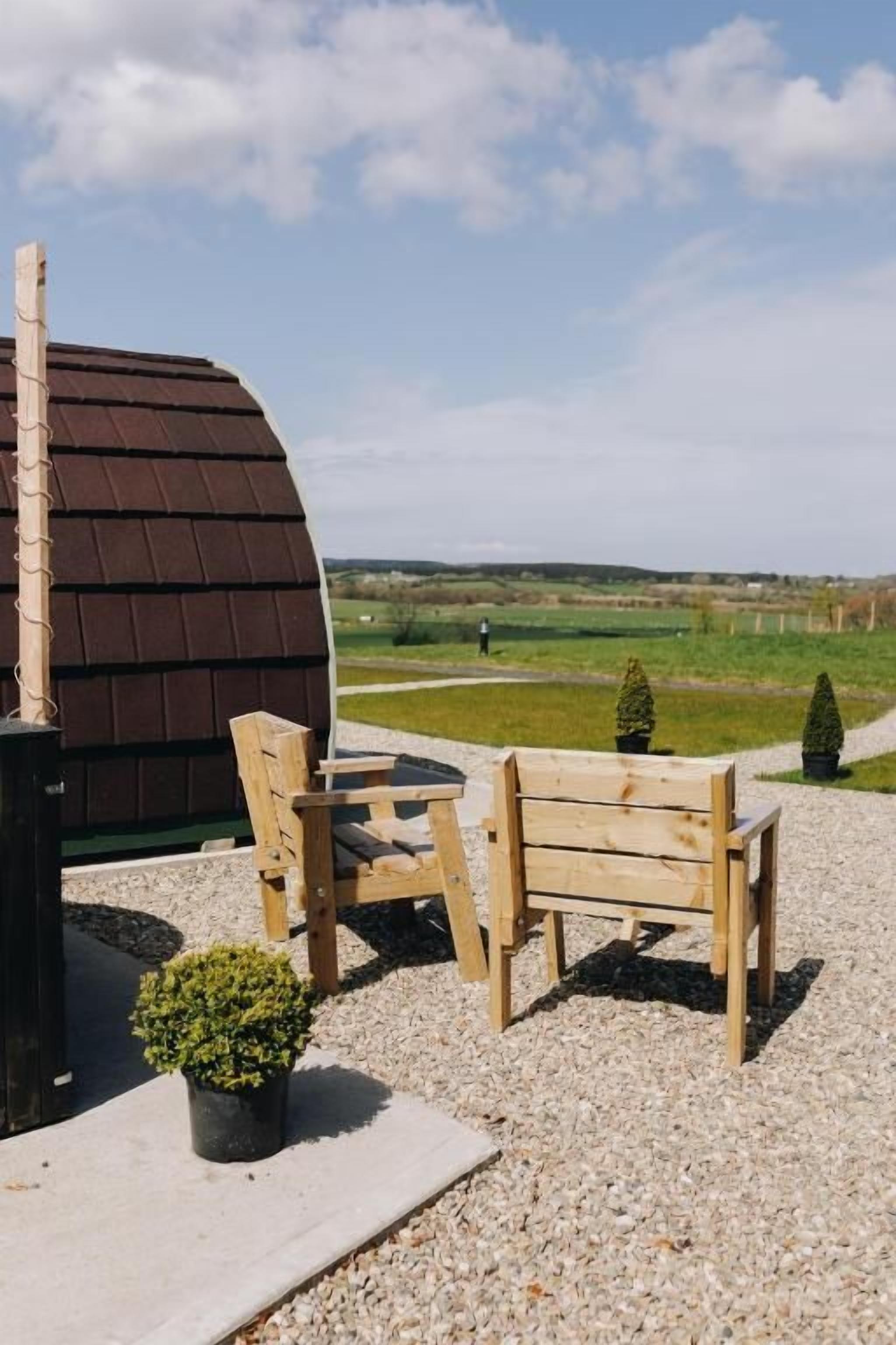A wooden bench and table set on a gravel surface with a view of a green field and a building with a brown roof.