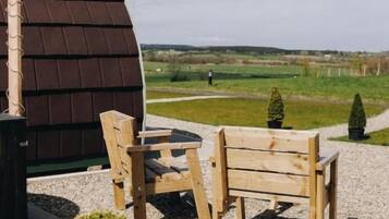 A wooden bench and table set on a gravel surface with a view of a green field and a building with a brown roof.
