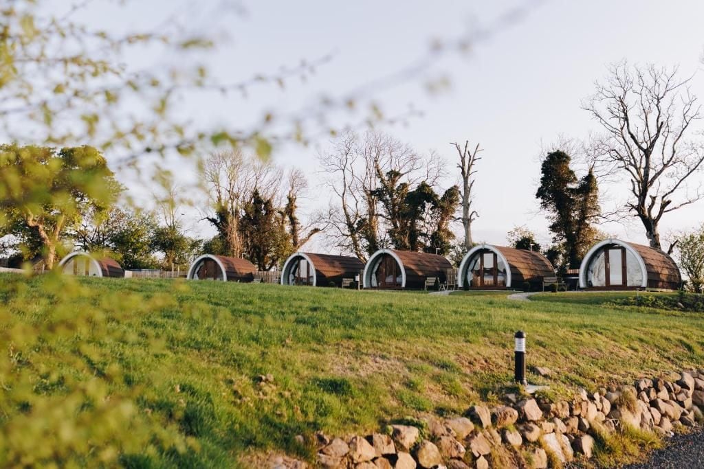 A row of rustic, barrel-shaped cabins with a stone wall in the foreground.