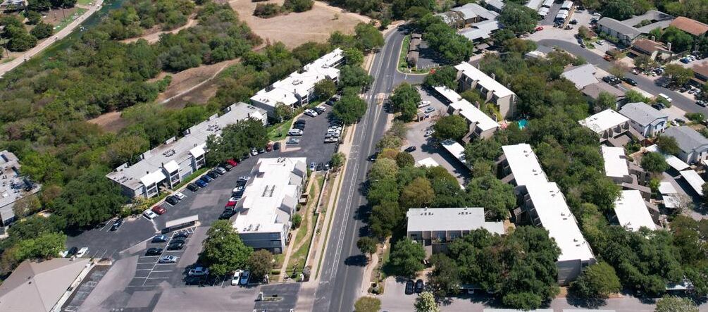 Vista aérea de um bairro residencial com casas separadas, uma avenida principal e um estacionamento.