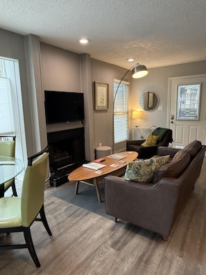 A living room with a fireplace, a flat-screen TV, a sofa, a coffee table, and a dining table with chairs.