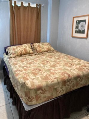 Un lit recouvert d’une couvre-lit à motifs floraux, un rideau marron et un tableau encadré accroché au mur.