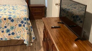 A bedroom with a wooden bed, a wooden dresser, a television, and a nightstand with a lamp.