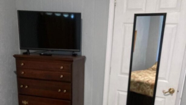 Een slaapkamer met een bed, een dressoir, een televisie en een deur met een spiegel.