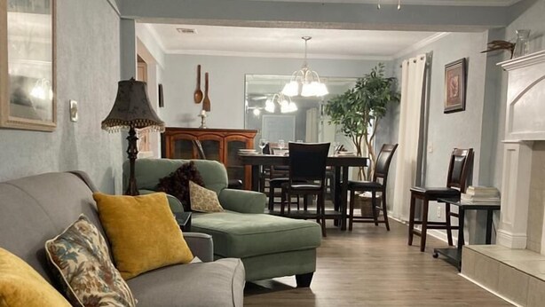 A living room with a grey sofa, yellow cushions, a dining area with a chandelier, and a ceiling fan.