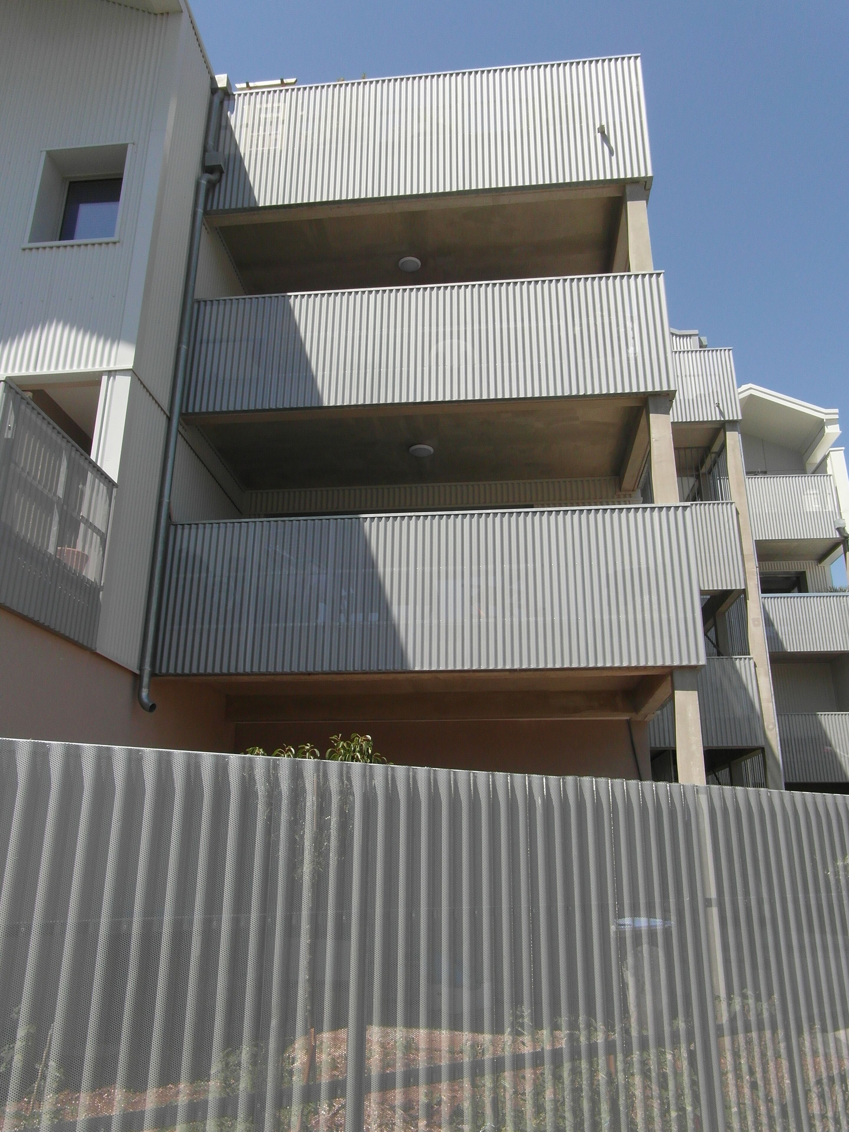 Ein mehrgeschossiges Gebäude mit einer wellenförmigen Metallfassade, Balkonen und einem sichtbaren Fenster.