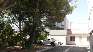 A parking area with a white building, trees, and parked cars. - Appt NEUF (2022) type 2 a 800 mètres ocean (La Rochelle)